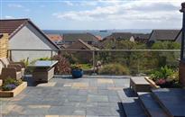 Glass balustrade has enhanced sea views from the sloping garden terrace in Kirkcaldy, Fife, Scotland. Glass panels on smart new patio provide wind protection.