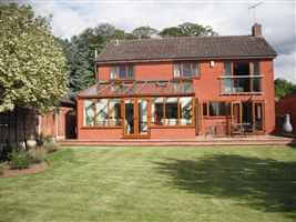 Wide Silver Juliet balcony at the back of a large brick house with conservatory and mowed lawns