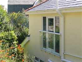 White Juliet balcony on the side wall of a house surrounded by plants and trees