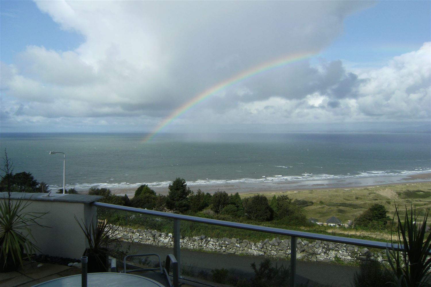 A Royal Chrome Aerofoil Glass Balustrade installed on a coastal home with a view of a rainbow