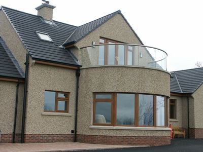 Curved Glass Semi-Frameless Glass Balustrade with bronze handrail on pebble dash house