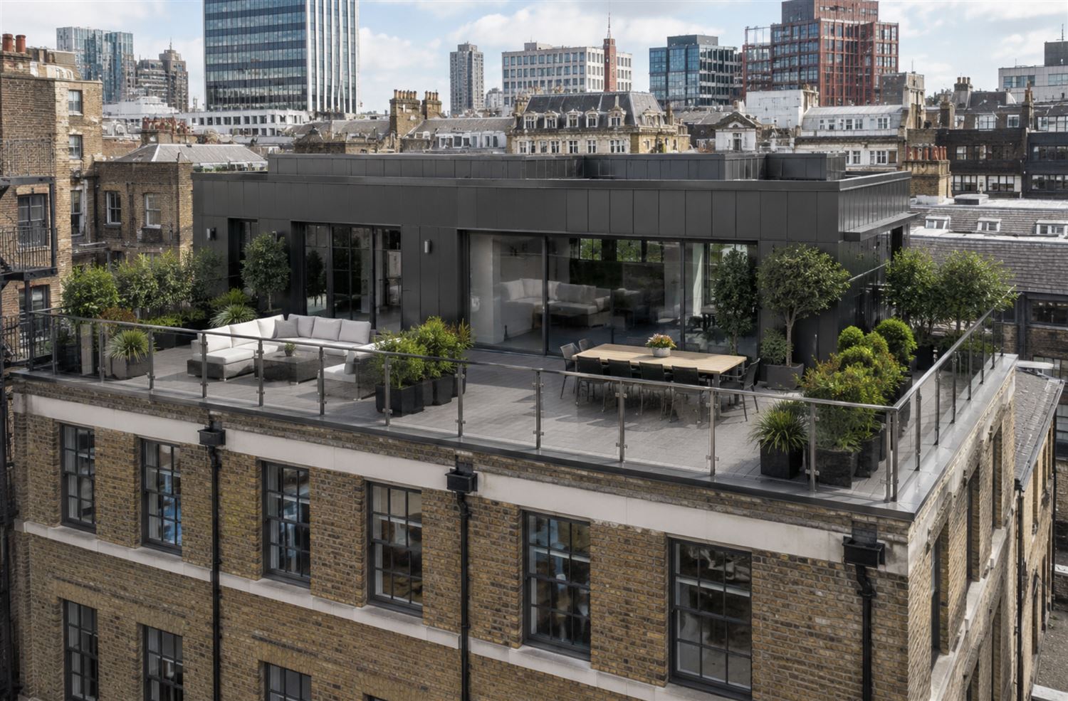 Retrofitted brick building in the UK featuring a modern rooftop terrace with composite decking, glass balustrades and contemporary outdoor seating.