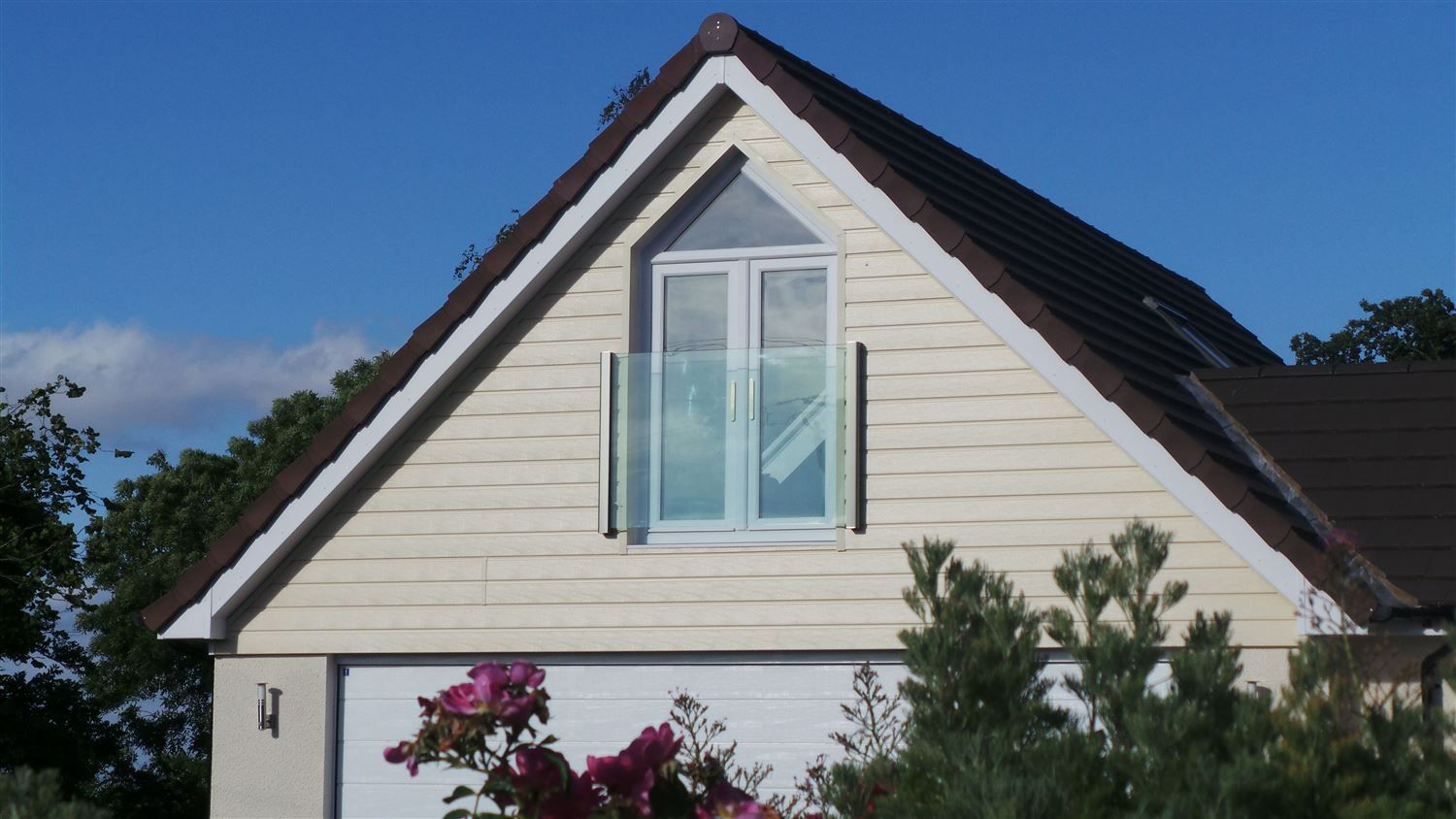 Frameless Juliet Balcony installed on a cream house with pretty pink flowers