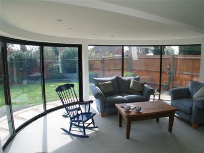inside view of a Curved Glass Patio looking out onto a small garden from a lounge with rocking chair