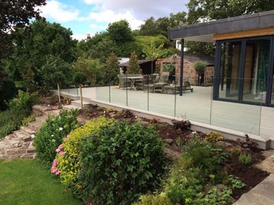 Frameless glass balustrade with the bottom rail sitting below the wooden decking, looking at the decking area and and house